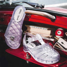 Clear jelly sandals on a red car dashboard with various items.