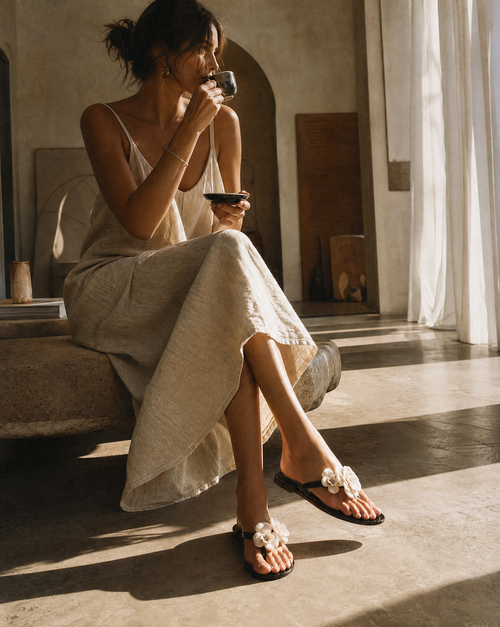 Woman in a white dress sitting on a stone floor, holding a cup.
